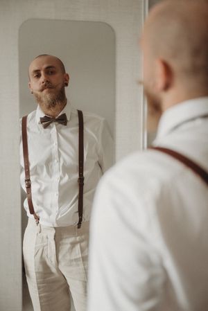 Reflection in mirror shows formal attire with brown suspenders and bow tie against white shirt.