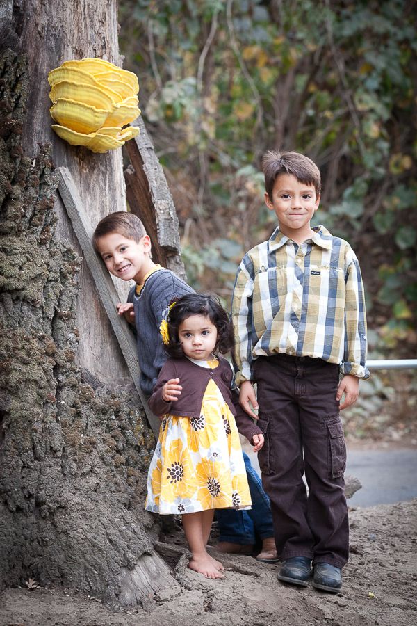 Two children in vintage-inspired yellow and plaid outfits play near a rustic stone wall outdoors.