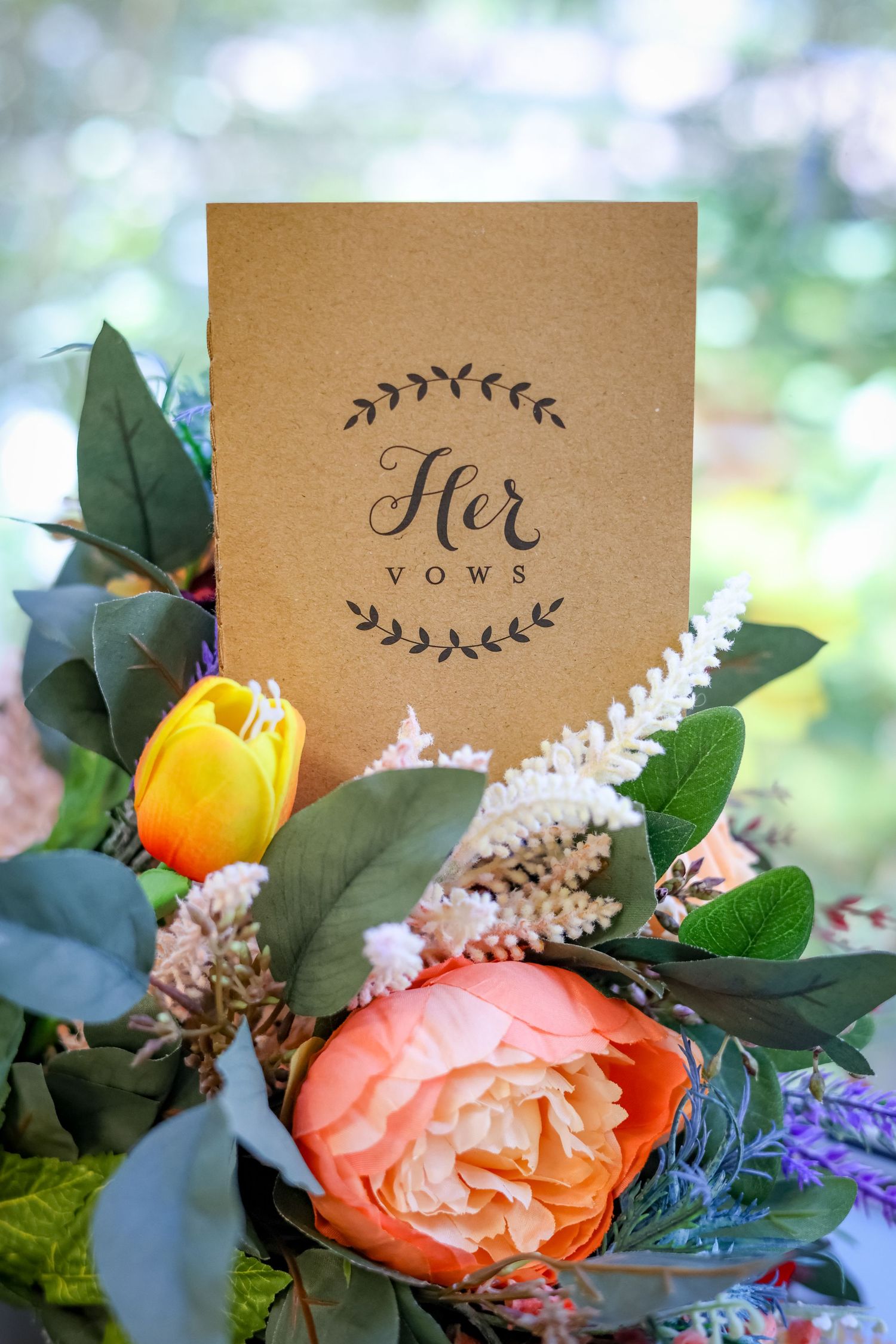 A kraft paper wedding vow card decorated with floral elements and calligraphy surrounded by colorful flowers.