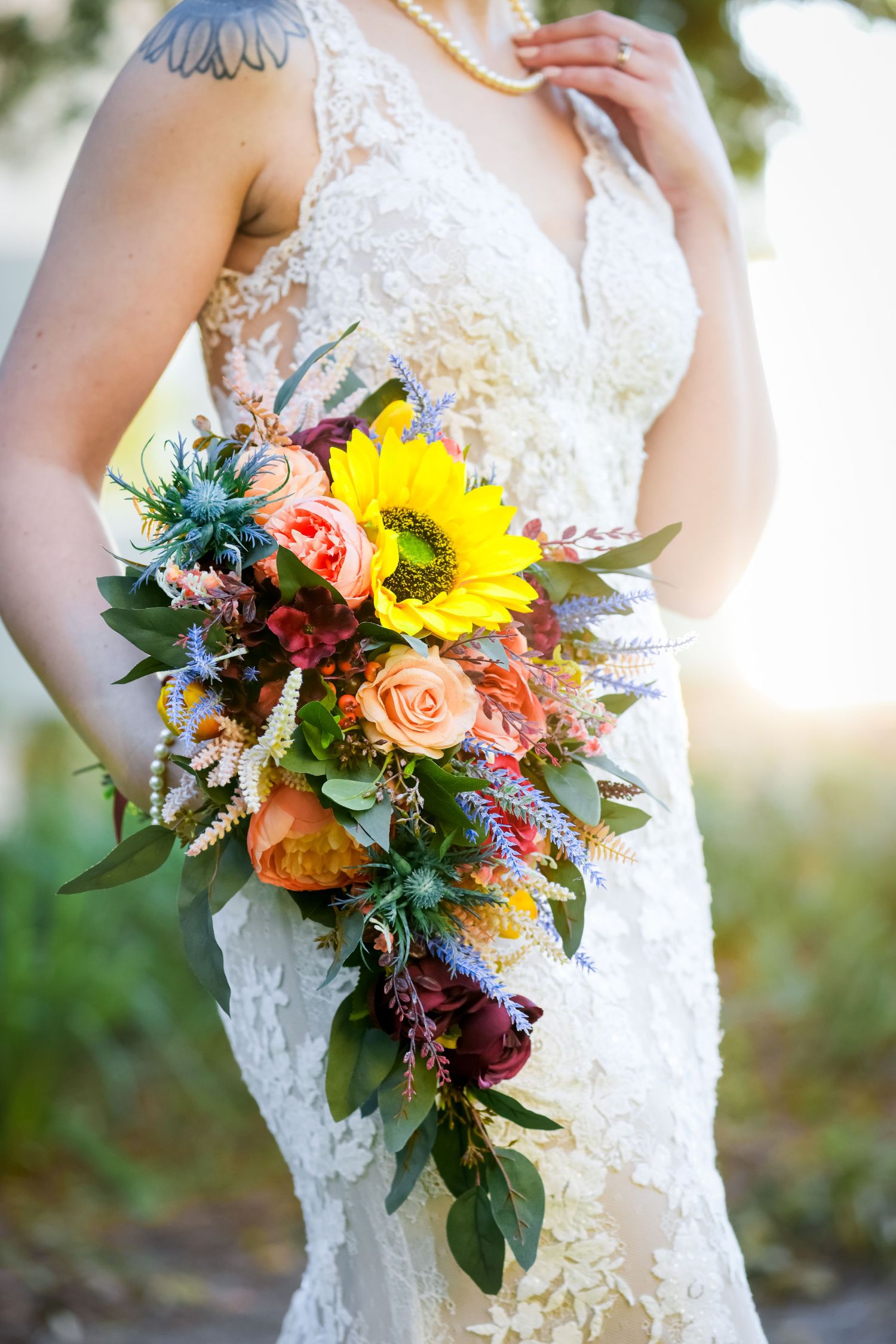 A bridal bouquet featuring vibrant sunflowers, roses, and greenery against a lace wedding dress.