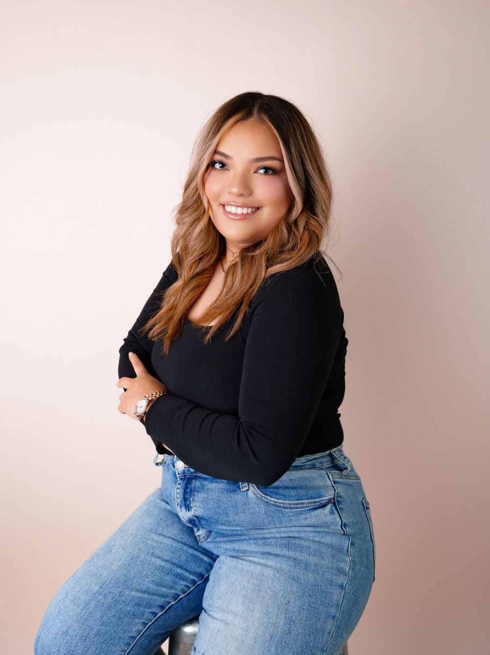Studio portrait against soft pink background wearing black top and blue jeans.