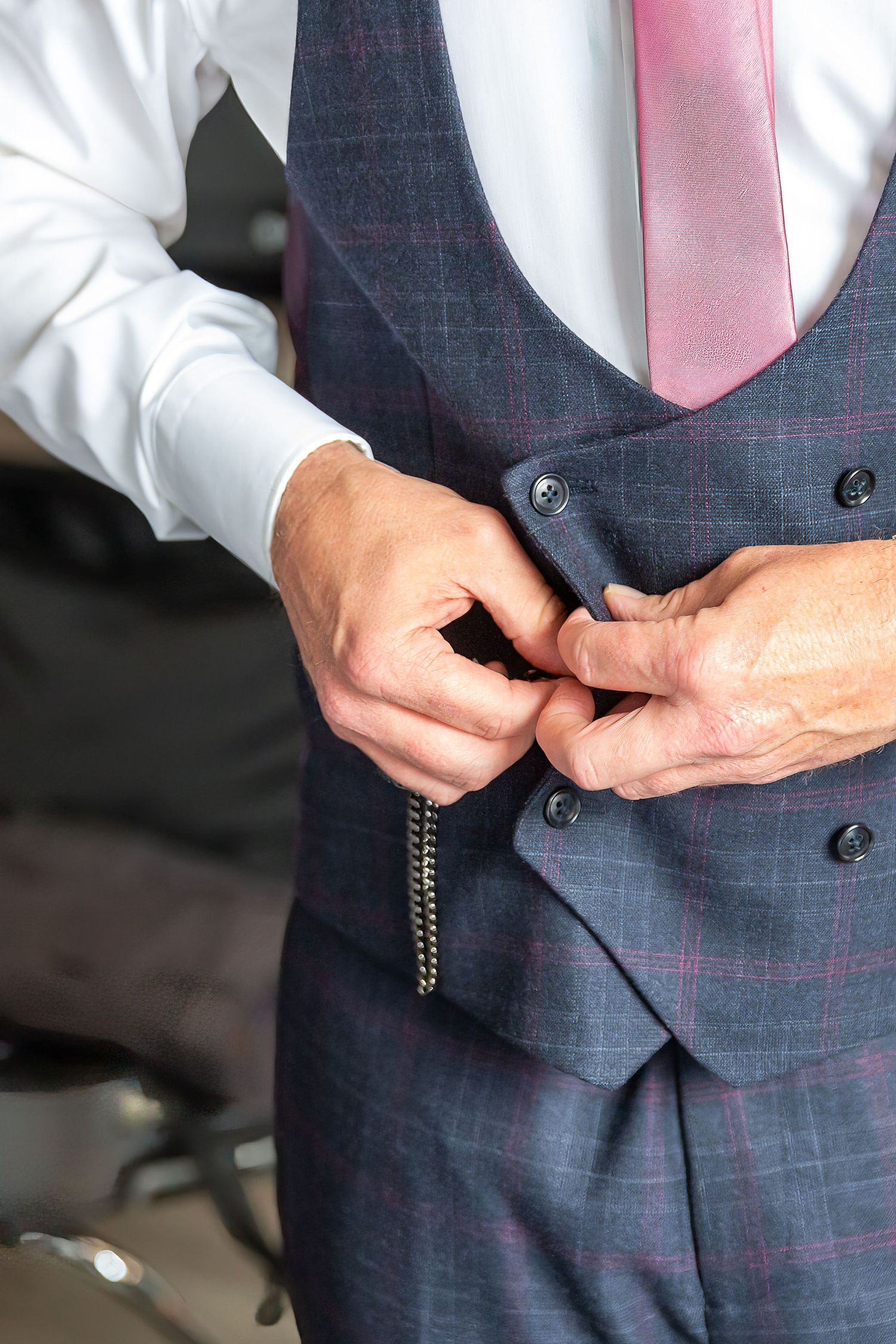 Close-up of the groom fastening a button on his waistcoat during the wedding morning. Liverpool Crowne Plaza hotel