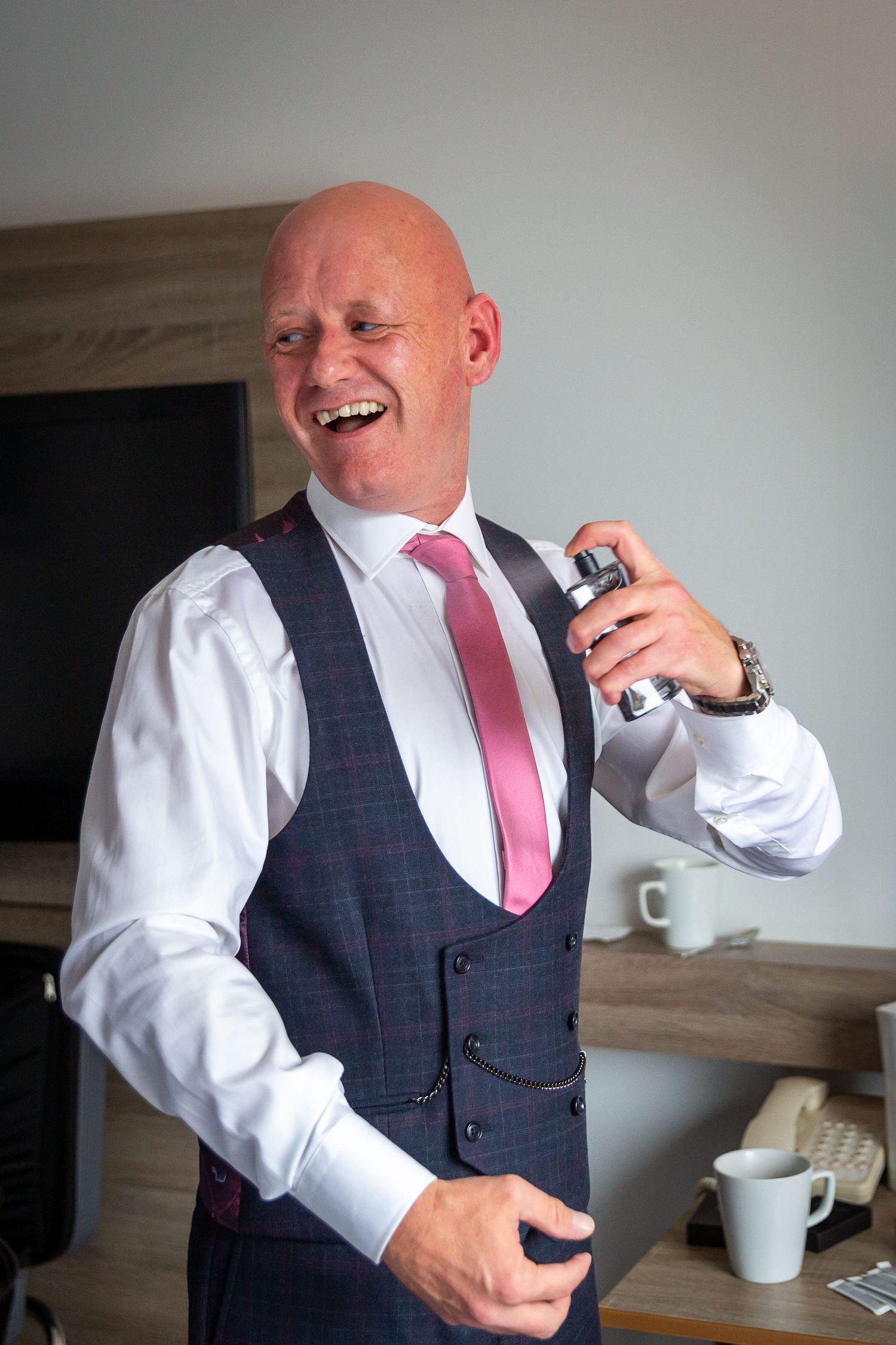 Groom laughing sprays his aftershave on the wedding morning. Liverpool wedding photographer. Stuart Morris Photography