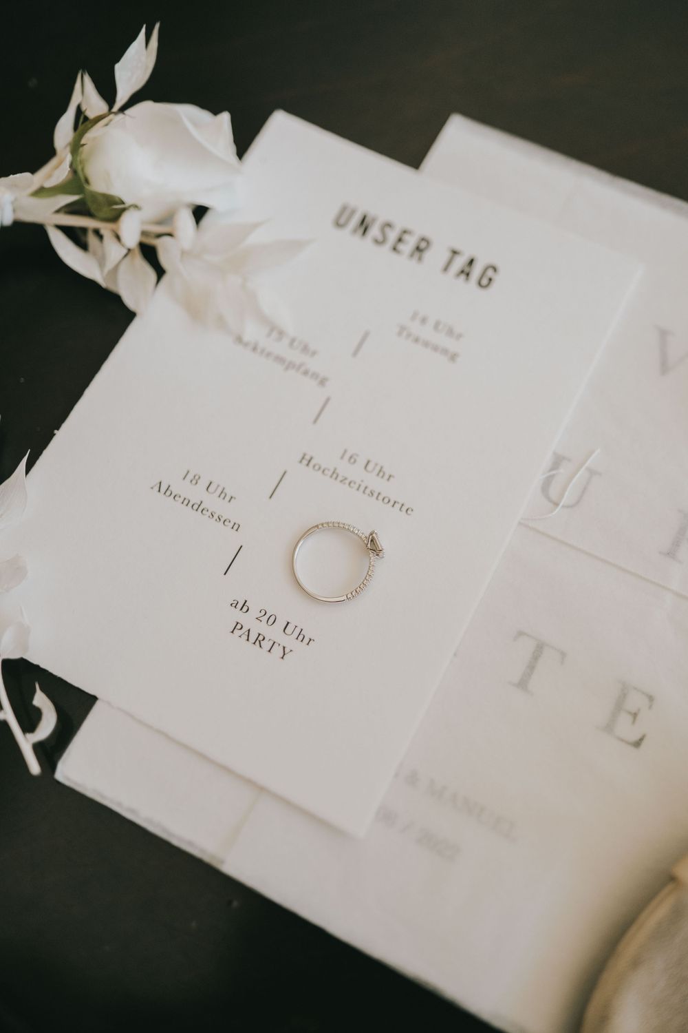 Wedding stationery with 'Unser Tag' text and engagement ring on dark background.