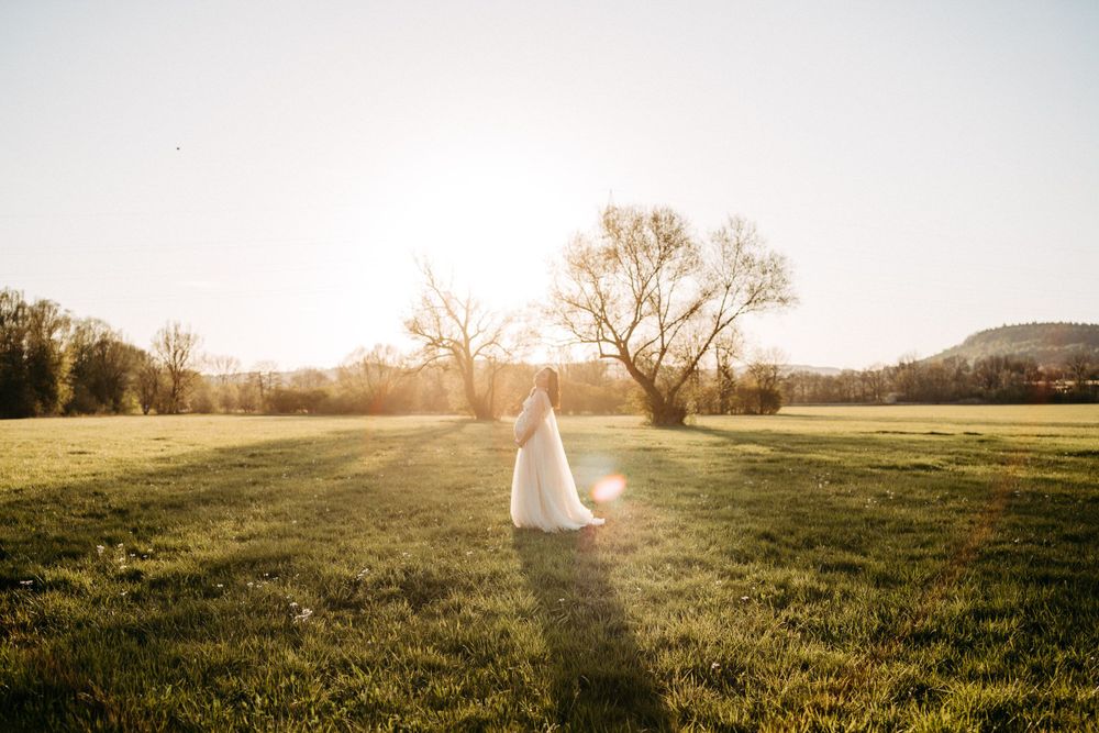 A dreamy golden sunset scene in a grassy field with a flowing white dress in silhouette.