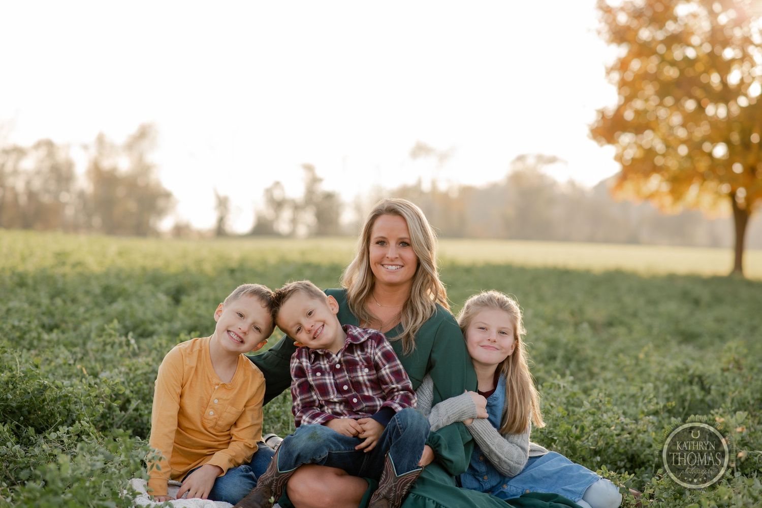 A relaxed outdoor family portrait in a green field with autumn trees in the background.