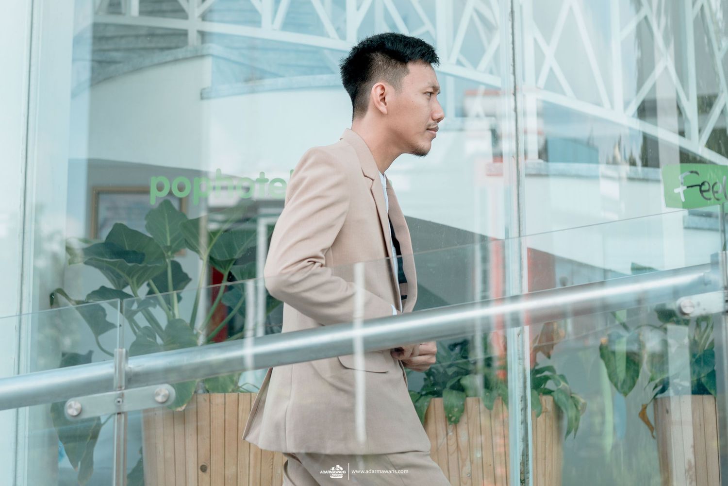 Side view of man in beige suit walking past glass windows in modern building.
