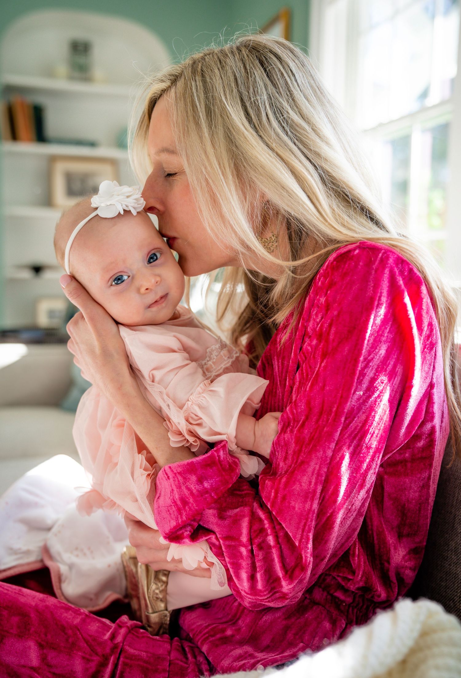 Tender moment between mother in pink velvet robe and baby in pink dress.