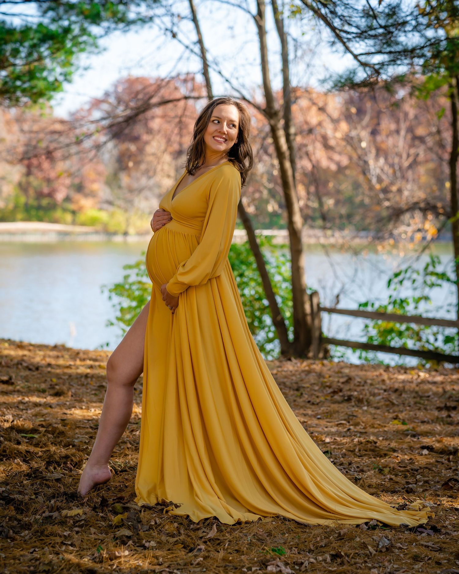 Maternity photo of woman in flowing yellow dress by autumn lake.