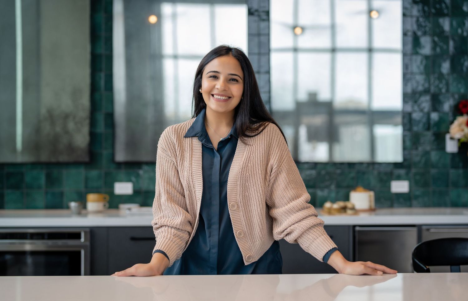 Professional woman in pink cardigan leaning on counter in modern office space.