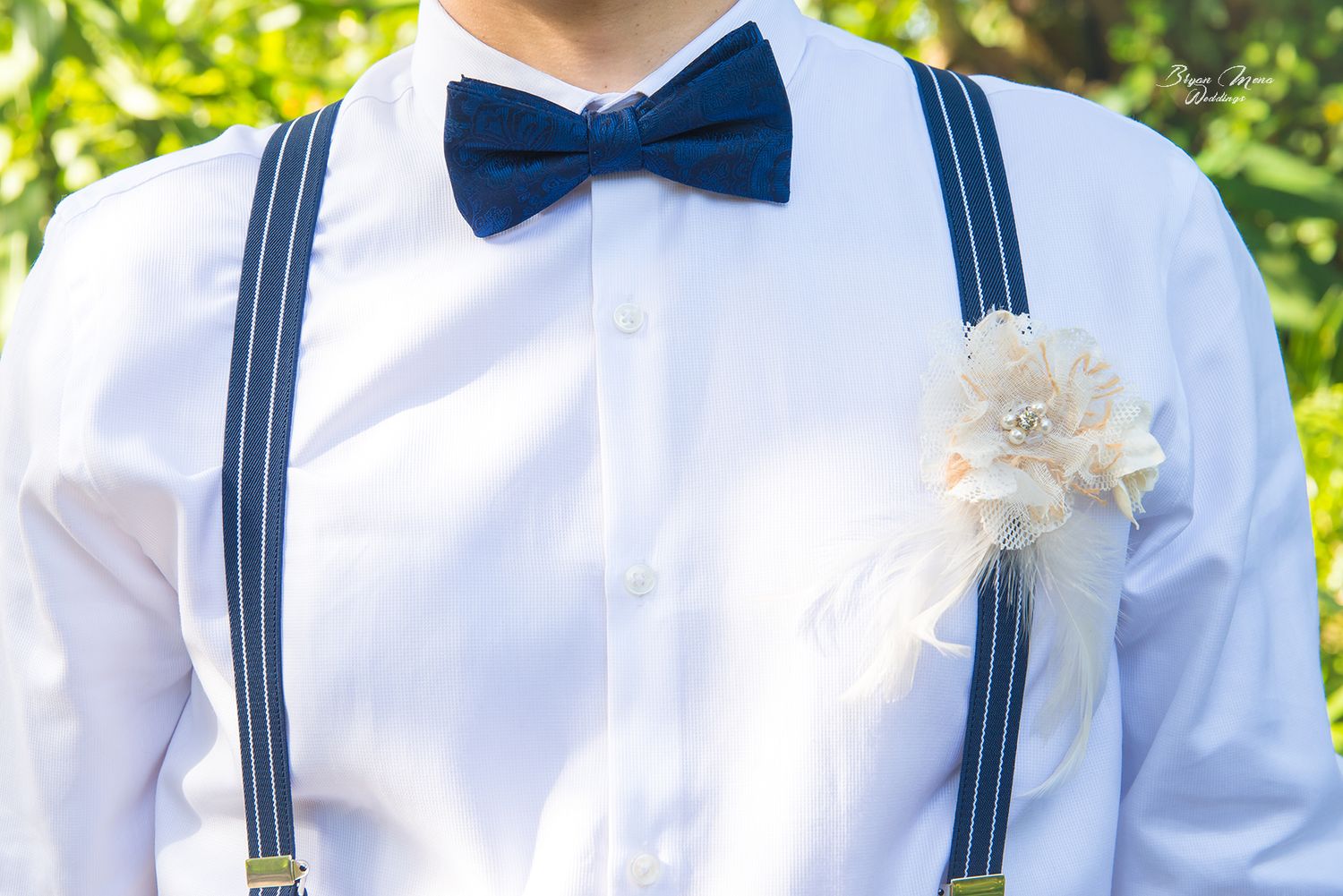 Navy suspenders and bow tie with white flower boutonniere on crisp white shirt.