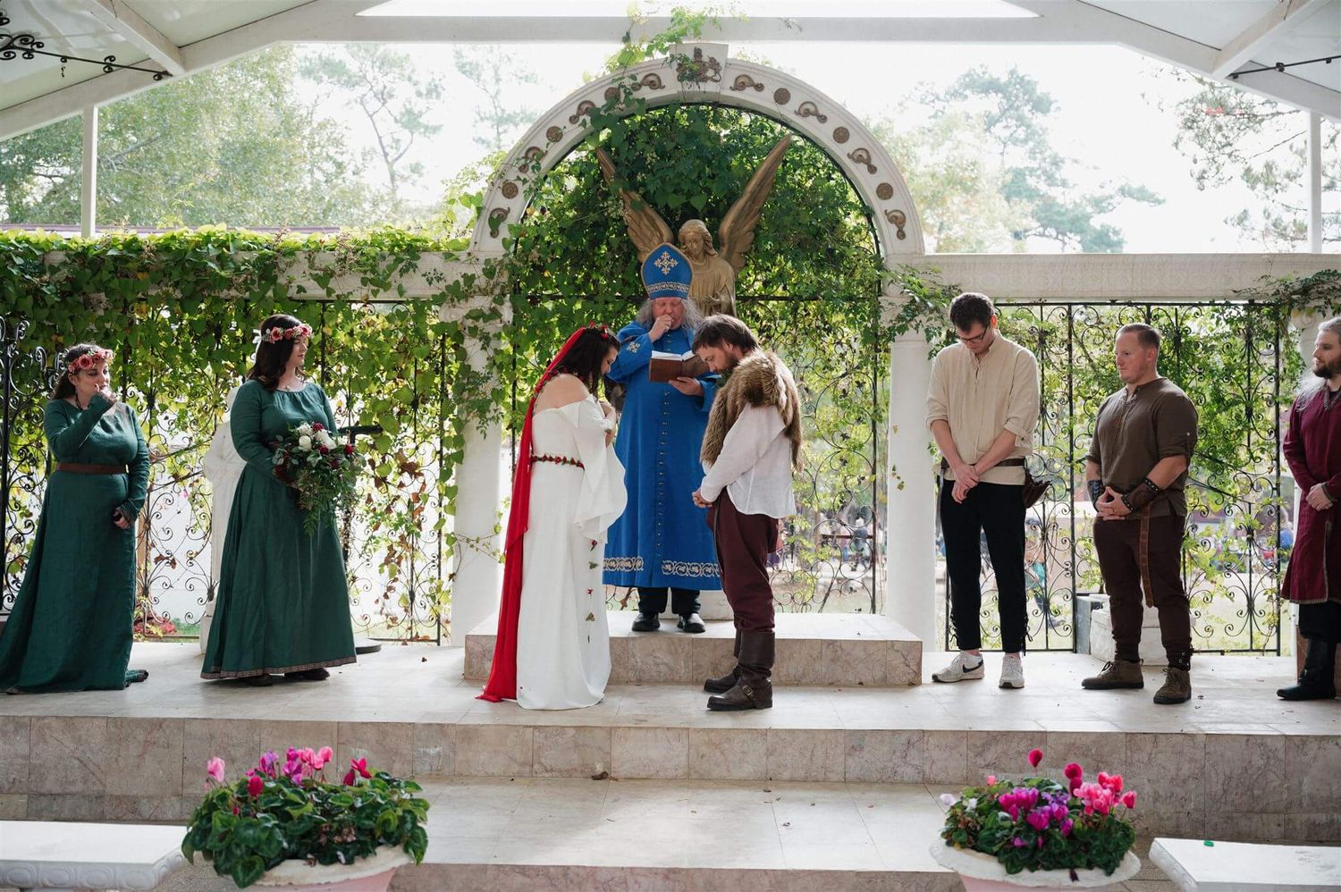 A wedding ceremony under a floral arch with attendees in medieval-style costumes and period dress.
