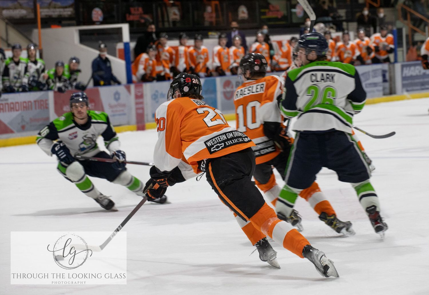 Ice hockey players in orange and green jerseys compete during intense game action.