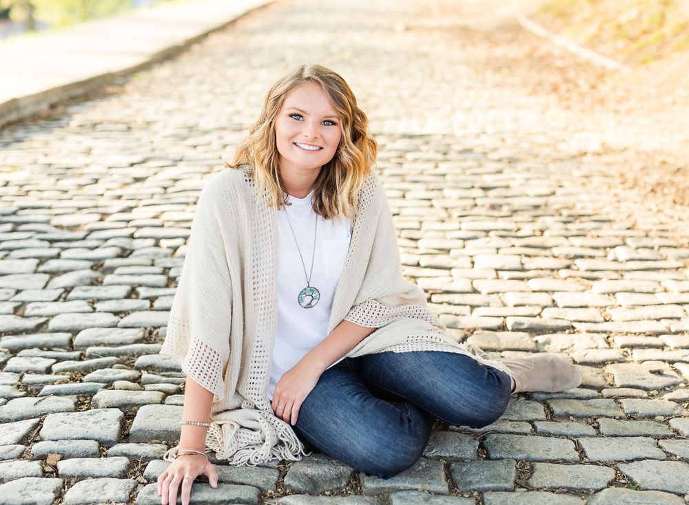 Person in casual cream sweater and jeans poses on cobblestone path during golden hour.