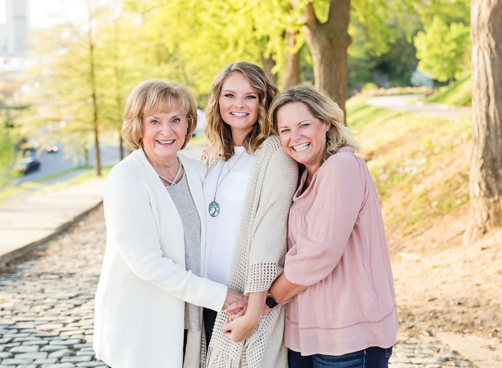 Three generations smiling and embracing outdoors on a sunny autumn day.