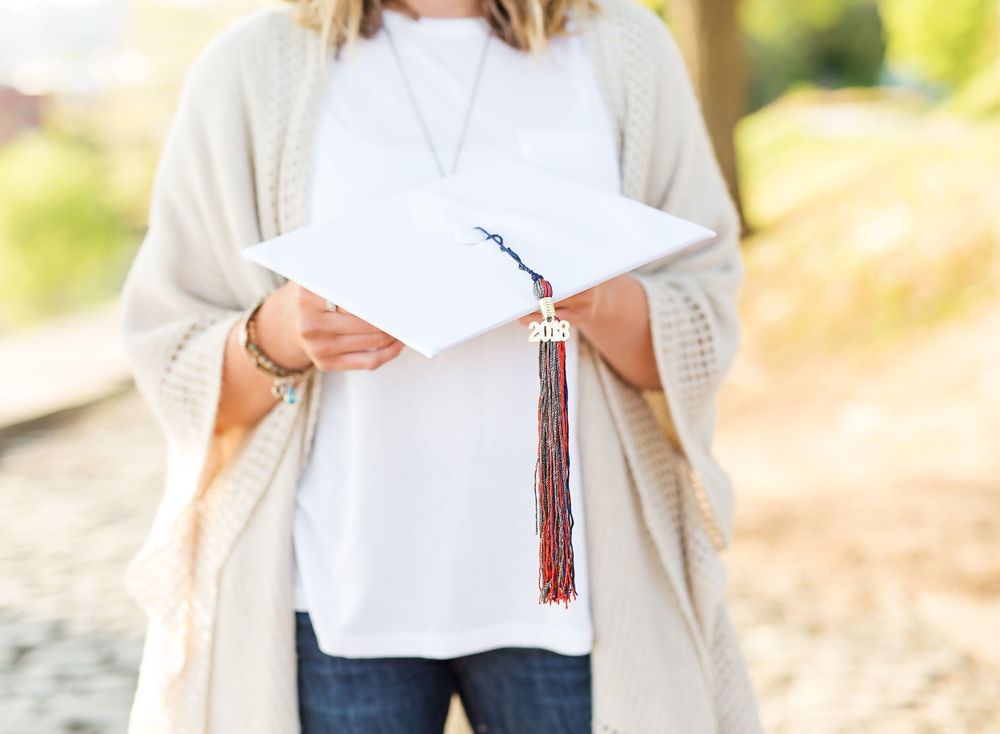 Detail shot of hands holding graduation tassel and diploma with cream cardigan in frame.