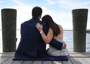 A couple sits close together on a wooden dock overlooking a peaceful waterfront view.