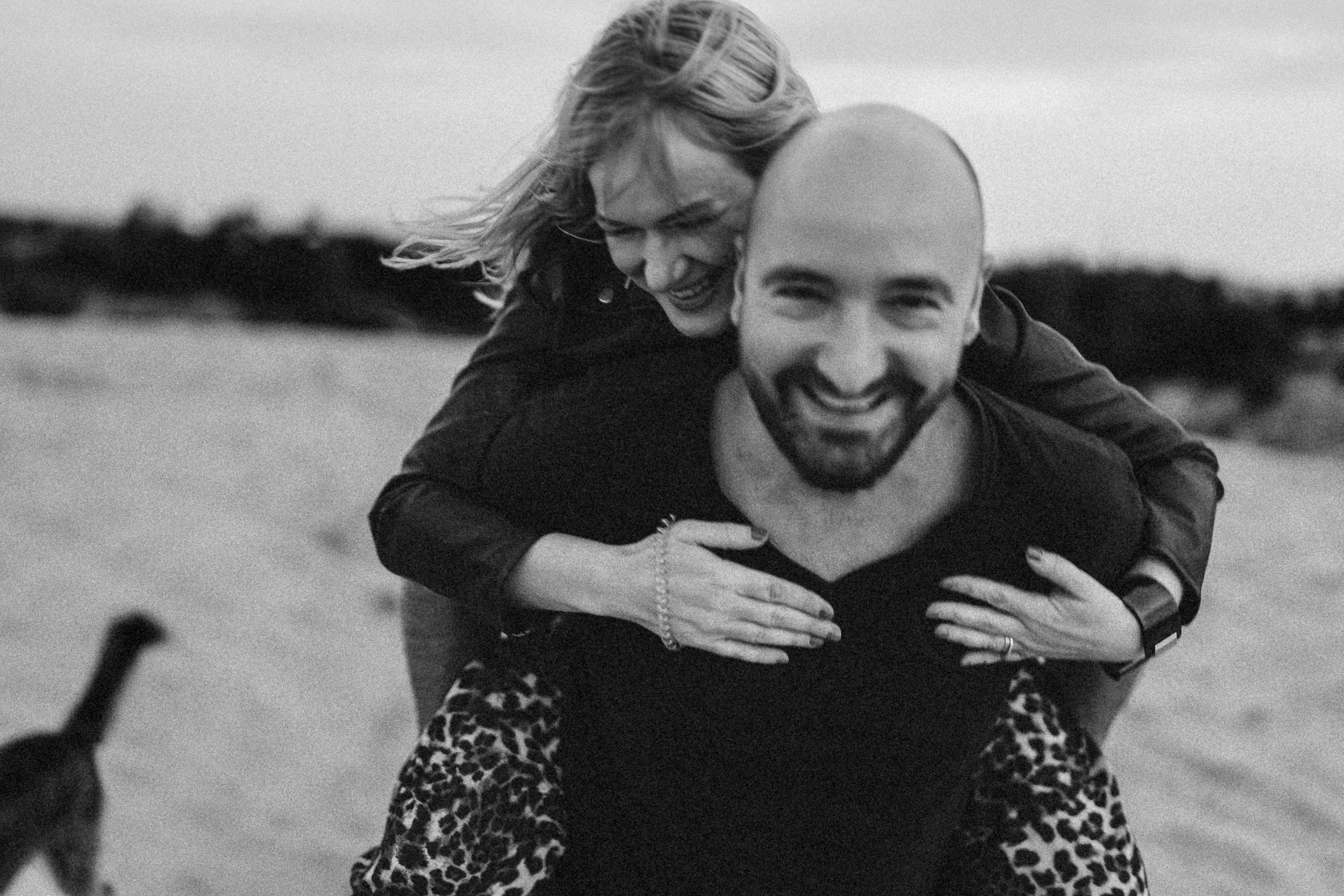 A joyful piggyback moment captured in black and white on a beach.