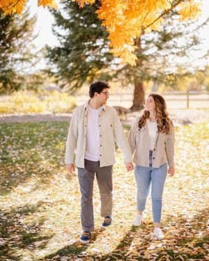 A couple walks through fallen autumn leaves in golden sunlight.
