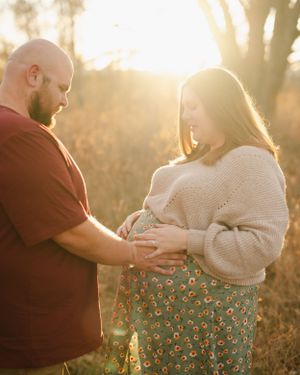 A maternity photo at sunset showing a couple in casual clothing.