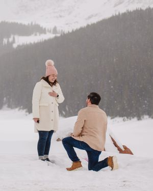 A winter proposal scene unfolds in the snowy mountains with someone kneeling.