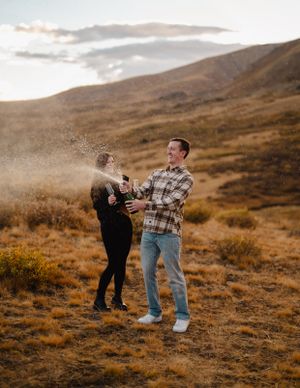 A playful couple dances together on a mountainside during golden hour.
