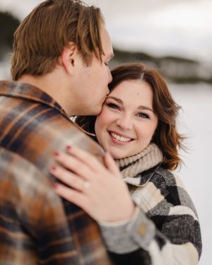 Cozy winter engagement photo with couple in plaid and knit wear sharing intimate moment.