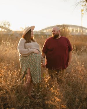 Two people sit together in a field during sunset with glowing golden light.