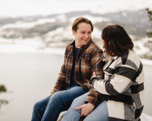 A couple sits together in winter clothing against a snowy mountain backdrop.