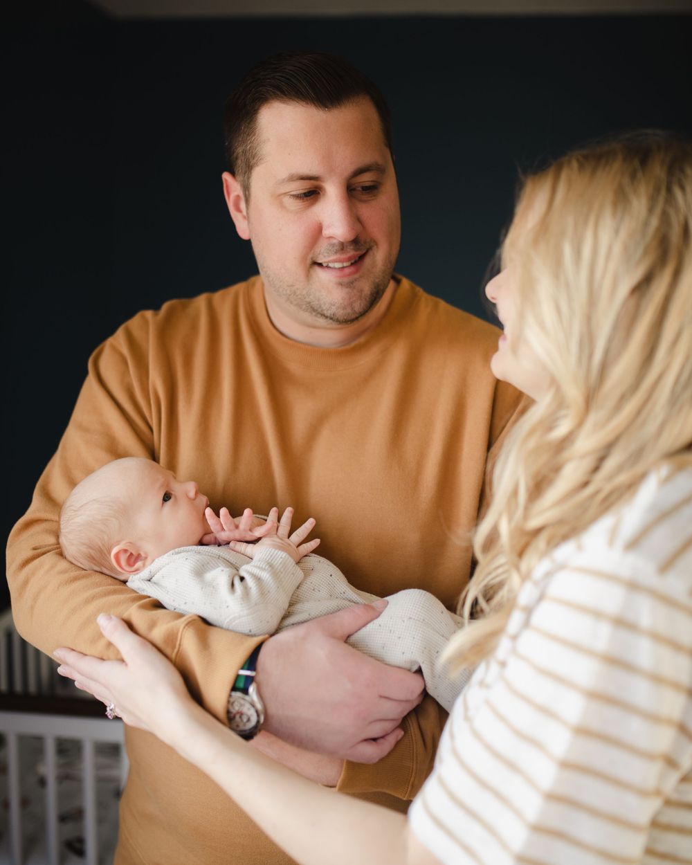 New parents share tender moment with newborn baby in warm lighting.