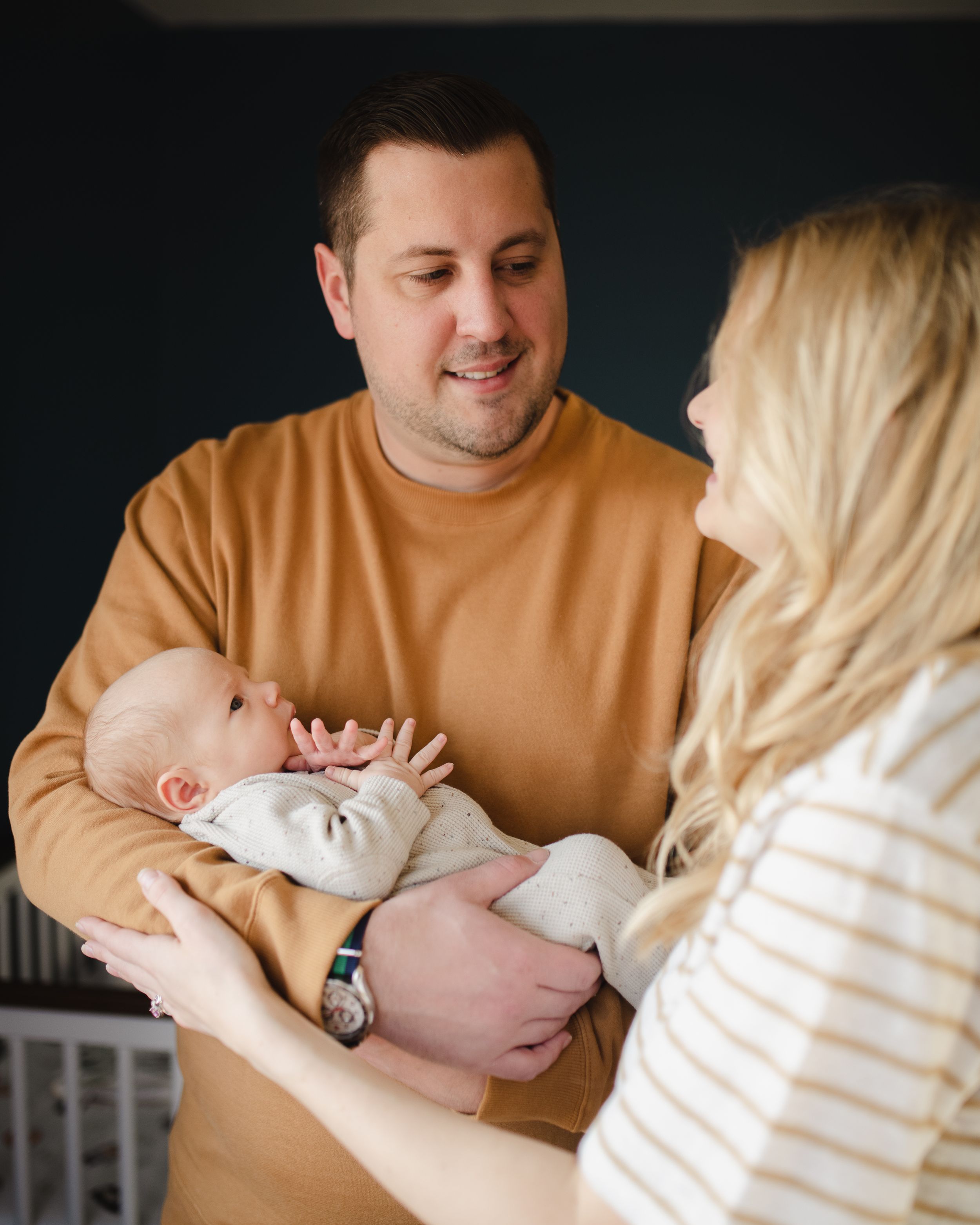New parents share tender moment with newborn baby in warm lighting.