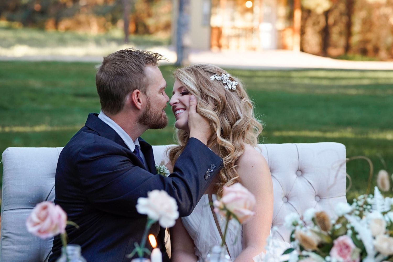 A couple sitting at a sweetheart table about to kiss on their wedding day at the Schnepf Farms Wedding Venue.