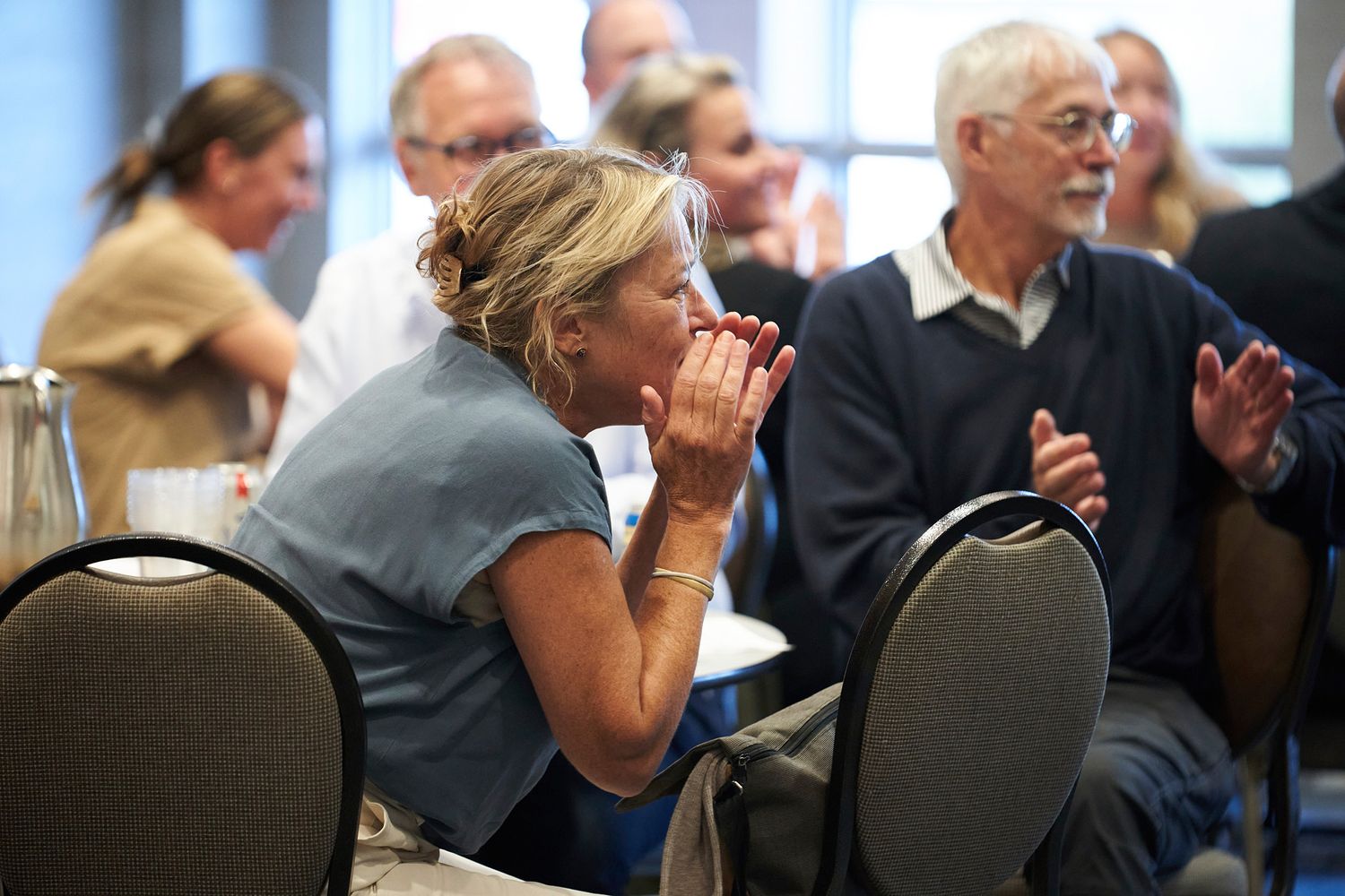 Audience members react enthusiastically during an event while seated in conference chairs.