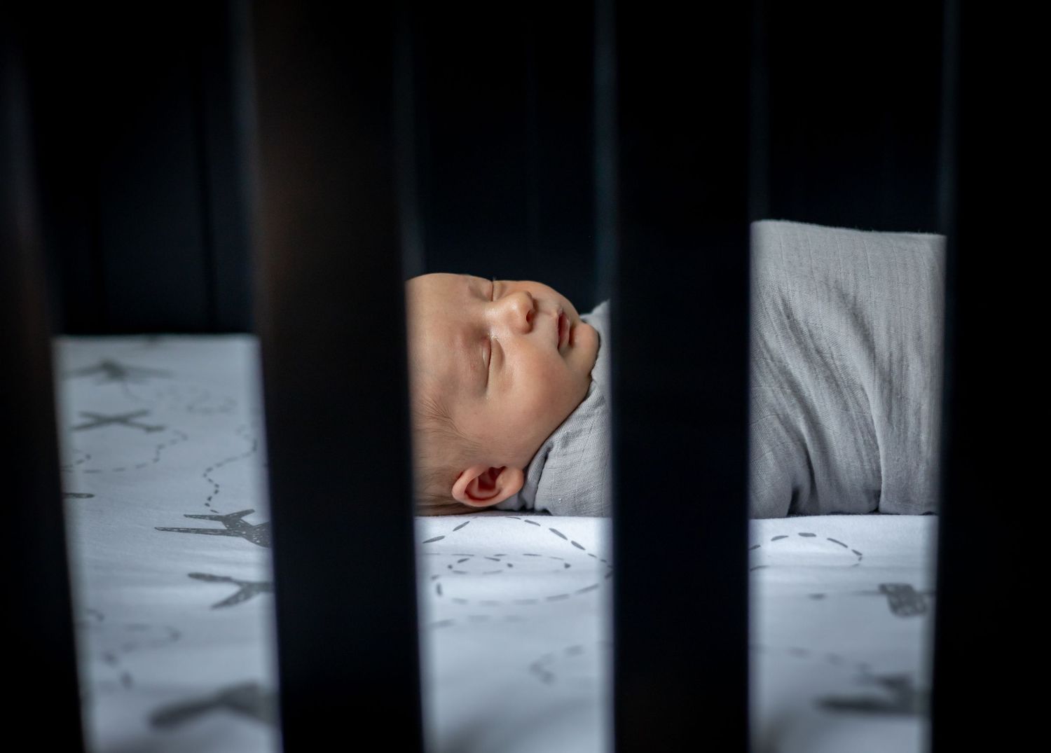 Close-up view through dark bars showing white bedding in soft focus.