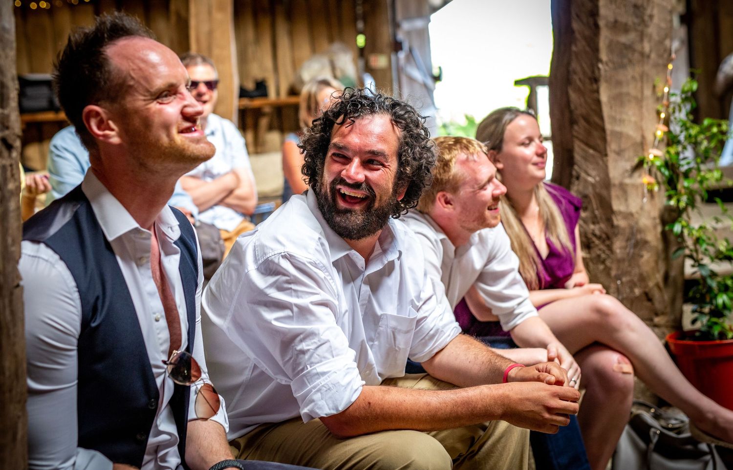 Wedding guests laugh and enjoy themselves during reception in rustic venue.