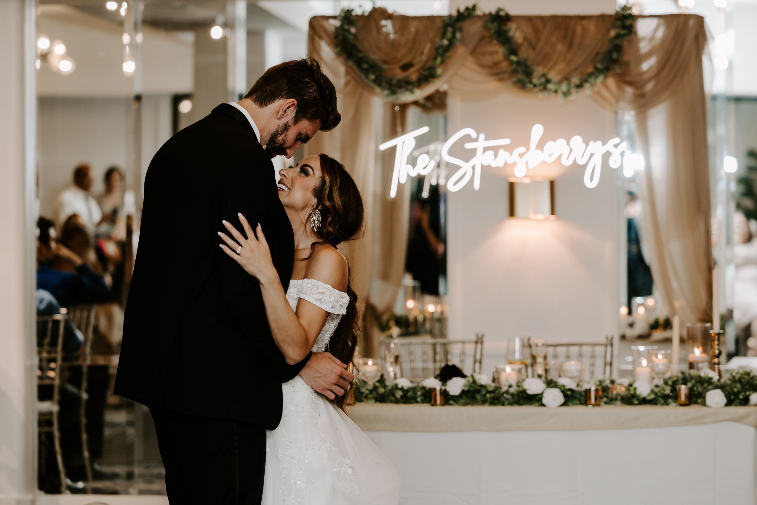A romantic wedding moment with neon signage and floral decor in an elegant indoor venue.