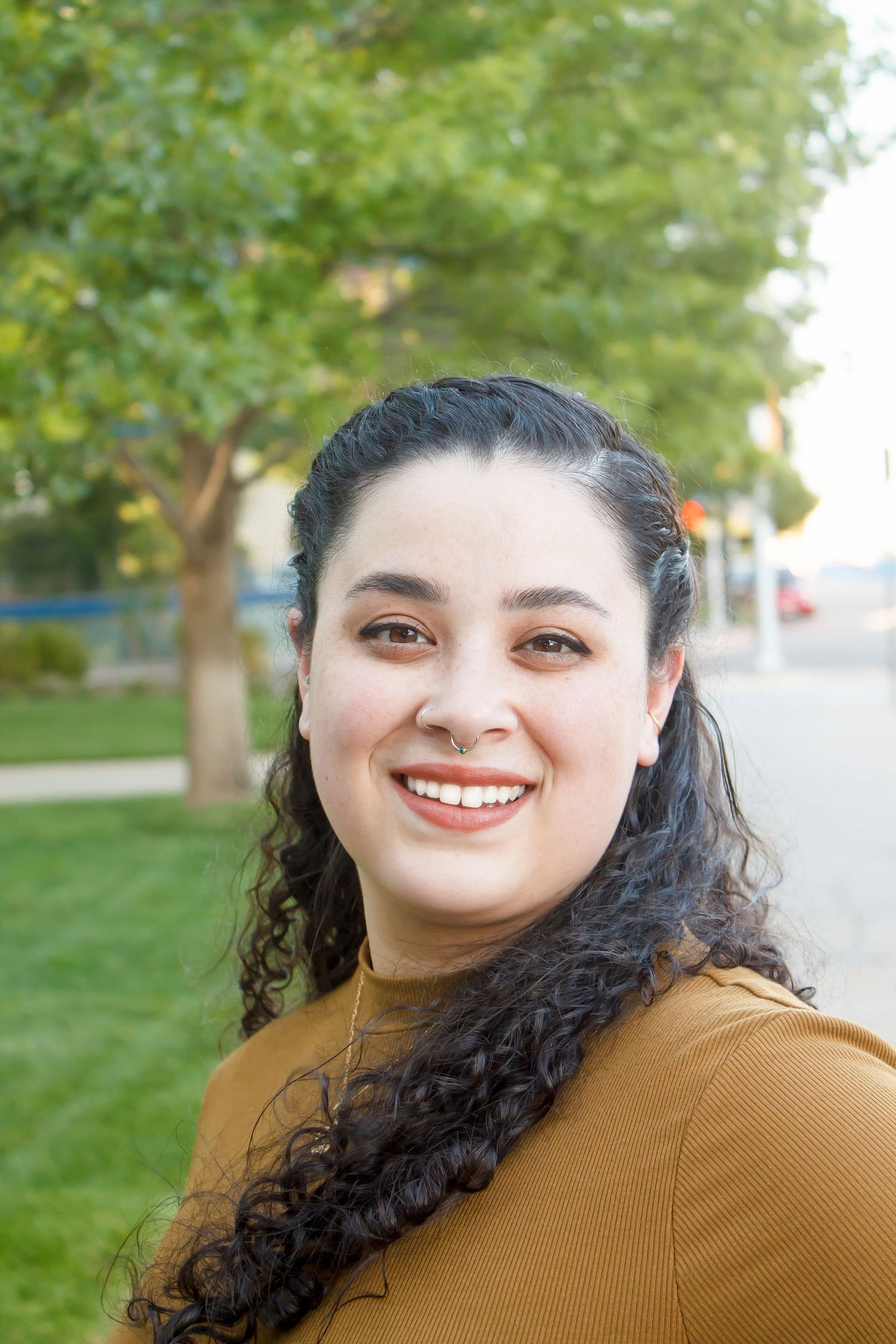 Close up outdoor portrait of someone in a mustard sweater with a bright smile.