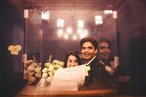Newlyweds smiling while holding their marriage certificate in warm lighting.