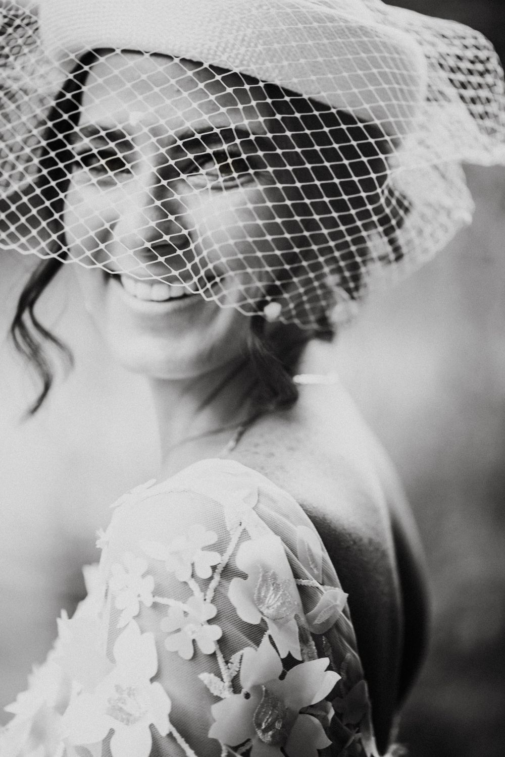 Black and white portrait showing delicate details of a birdcage veil and floral dress.