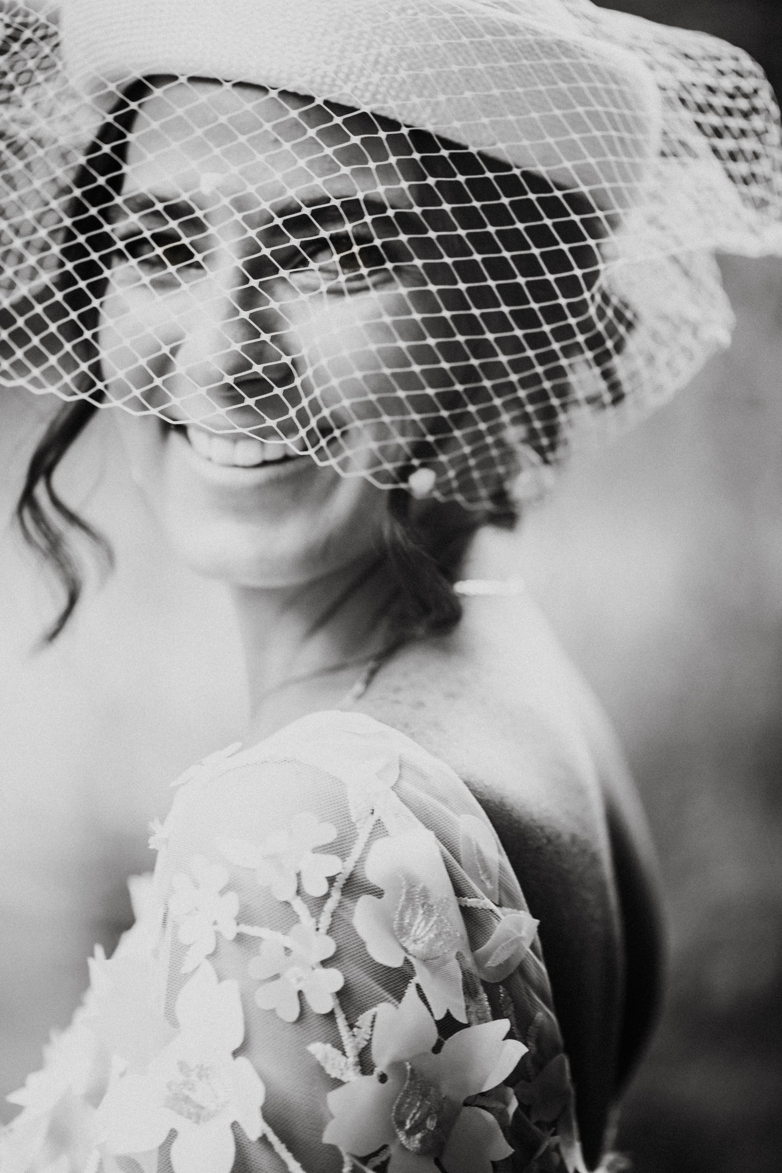 Black and white portrait showing delicate details of a birdcage veil and floral dress.
