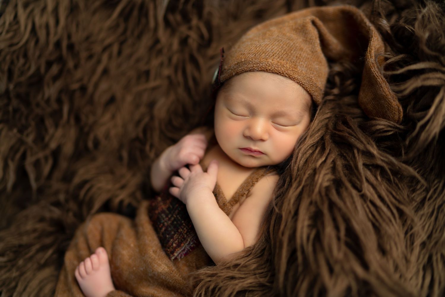 Artistic newborn portrait on textured brown fabric with matching hat.