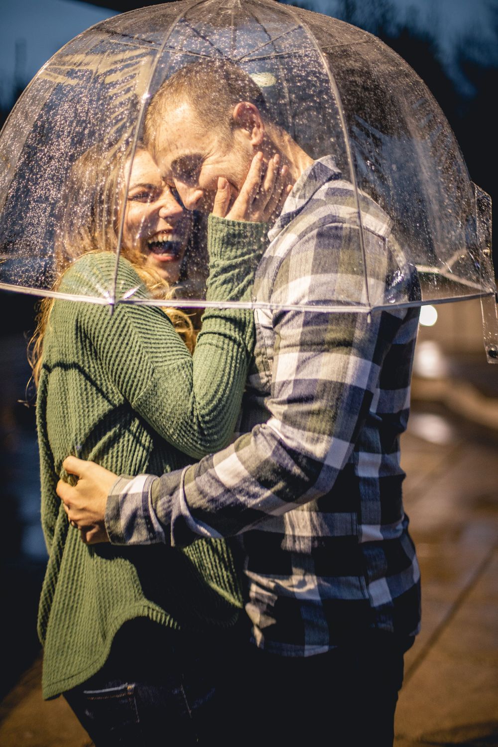 A joyful couple laughing together under a clear umbrella on a rainy day.