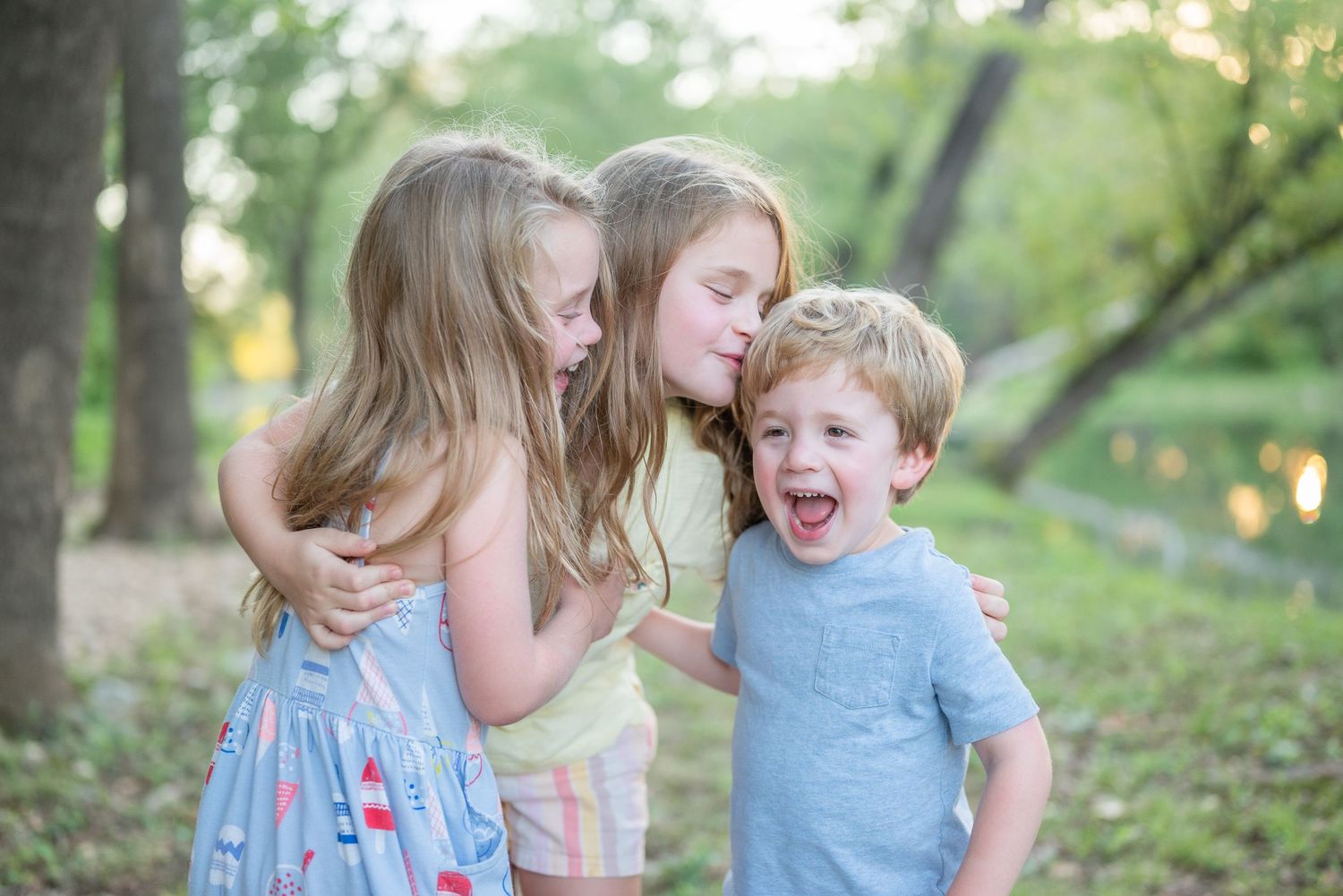 Three playful siblings share a candid moment together outdoors in natural lighting.