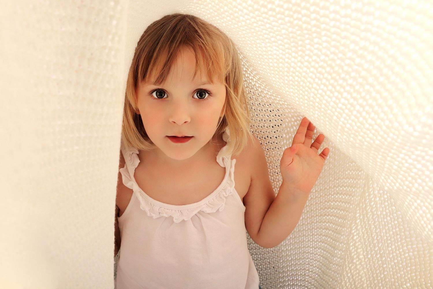 Enfant en débardeur blanc, en dessous d'une couverture texturez crème.