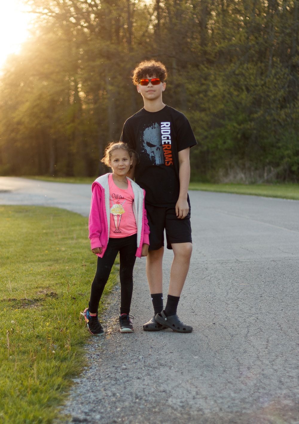 Siblings standing on path during golden hour sunset.