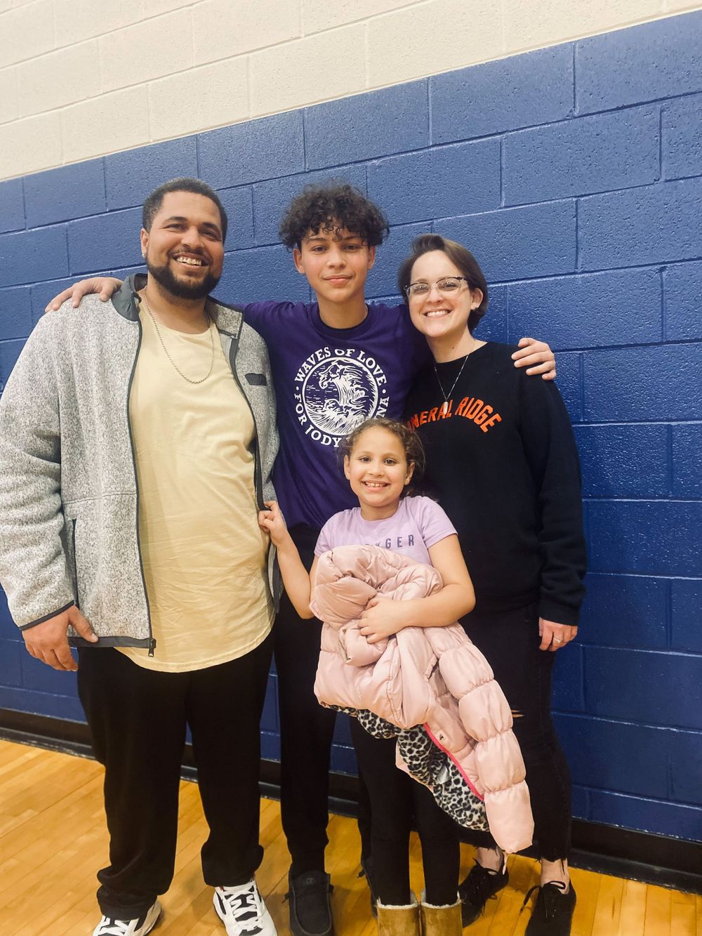 Family group poses together against blue wall in gymnasium setting.