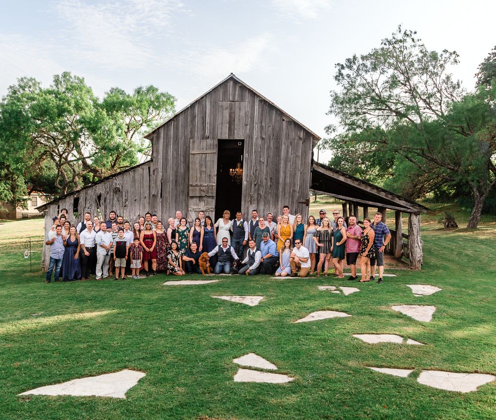 large wedding party taking a group photo in front of a old rustic barn