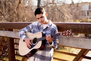 A-High-School-Senior-standing-on-a-bridge-playing-a-guitar-in-Alma-Michigan,