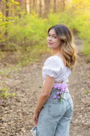 A spring portrait in distressed jeans and white top along a wooded trail.