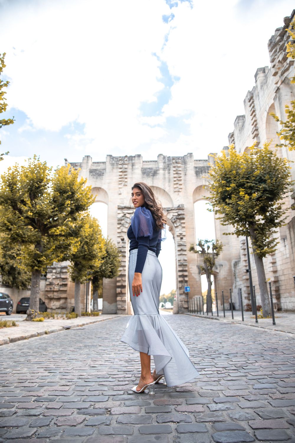 Flowing blue and white outfit styled against historic stone architecture and cobblestone street.